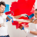 Young funny couple are doing repair at home and painting a wall with roller.